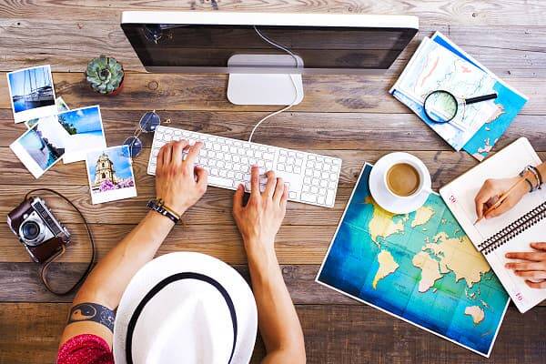 Reiseplanung mit dem AsiaGo Reiseplaner Person sitzt am Schreibtisch und plant eine Reise mit Karte, Laptop, Notizbuch und Urlaubsfotos