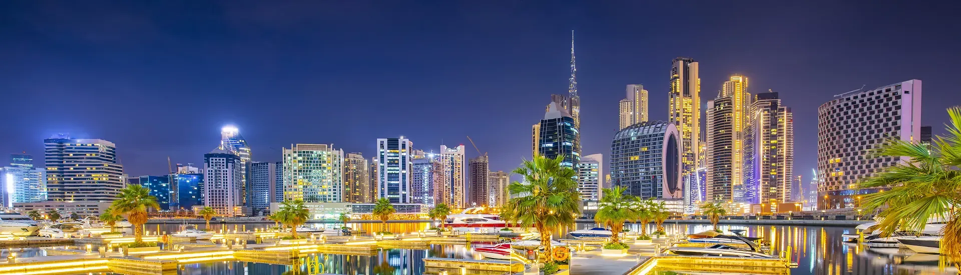 Beleuchtete Skyline der Dubai Marina mit Palmen und Yachten im Vordergrund – AsiaGo