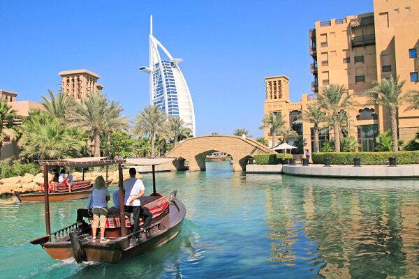 Reisepakete Dubai buchen – Highlights & Luxusurlaub mit AsiaGo Traditionelles Holzboot auf Wasserkanal mit Blick auf moderne Skyline und Burj Al Arab in Dubai – AsiaGo