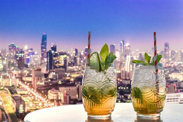 Zwei Cocktails mit Minze auf einer Rooftop-Bar mit Blick auf Bangkoks Skyline bei Nacht