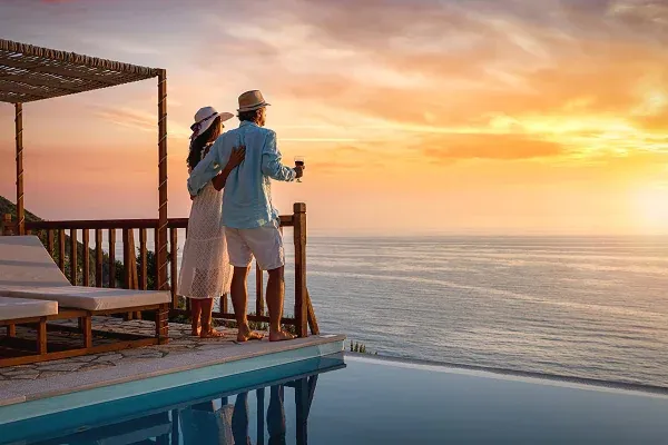 Paar genießt den Sonnenuntergang auf einer Hotelterrasse mit Infinity-Pool und Blick auf das Meer während einer Hotelverlängerung nach der Kreuzfahrt.