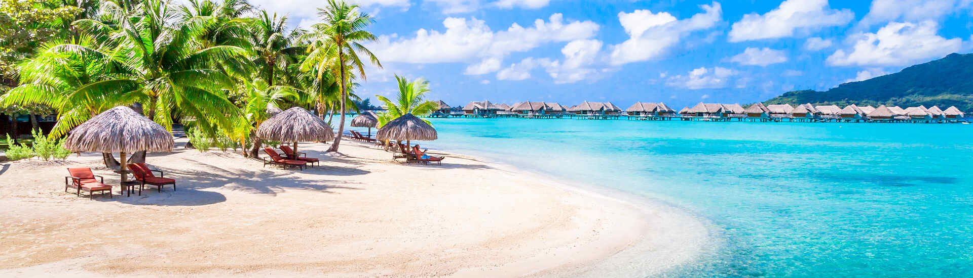 Sandstrand mit Palmen, Liegestühlen und Wasserbungalows über türkisblauem Meer in tropischer Umgebung