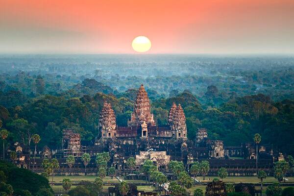 Blick auf den Tempel Angkor Wat in Kambodscha bei Sonnenaufgang, umgeben von tropischem Wald und historischer Tempelanlage.