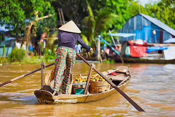 Person mit Strohhut rudert ein Holzboot im Mekong-Delta in Vietnam bei tropischer Vegetation