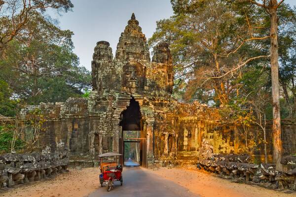 Historisches Steintor von Angkor Thom im Angkor-Park in Kambodscha, umgeben von tropischem Wald und traditionellem Tuk-Tuk auf der Zufahrtsstraße.