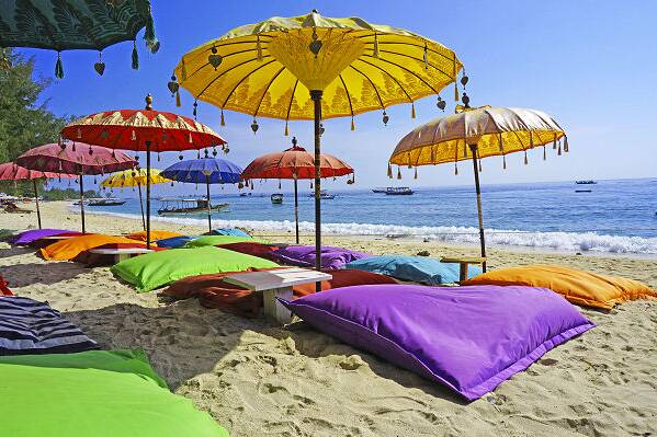 Bunte Strandliegen und Sonnenschirme an einem tropischen Strand in Indonesien beim Inselhopping