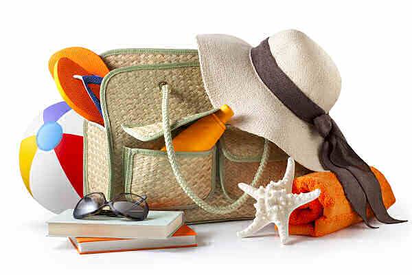 Strandtasche mit Sonnenhut, Handtuch, Sonnenbrille und Ball – Symbol für Reiseplanung