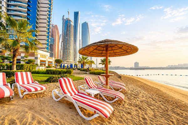Strand in Abu Dhabi mit Liegen, Palmen und moderner Skyline
