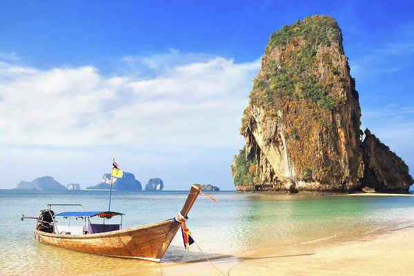 Longtailboot am Strand von Krabi mit türkisfarbenem Meer und markanten Kalksteinfelsen beim Inselhopping in Thailand