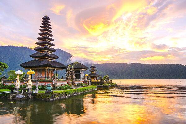Traditioneller balinesischer Tempel am See bei Sonnenuntergang auf Bali, Indonesien, mit Spiegelungen im Wasser und Bergkulisse im Hintergrund.