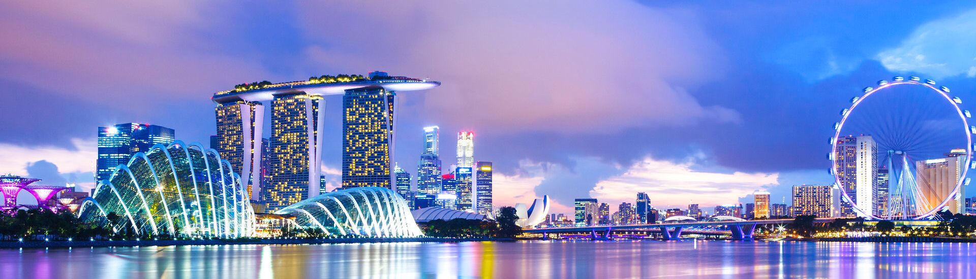 Marina Bay in Singapur mit dem Marina Bay Sands Hotel, den Gewächshäusern der Gardens by the Bay und dem Singapore Flyer bei Abendbeleuchtung.