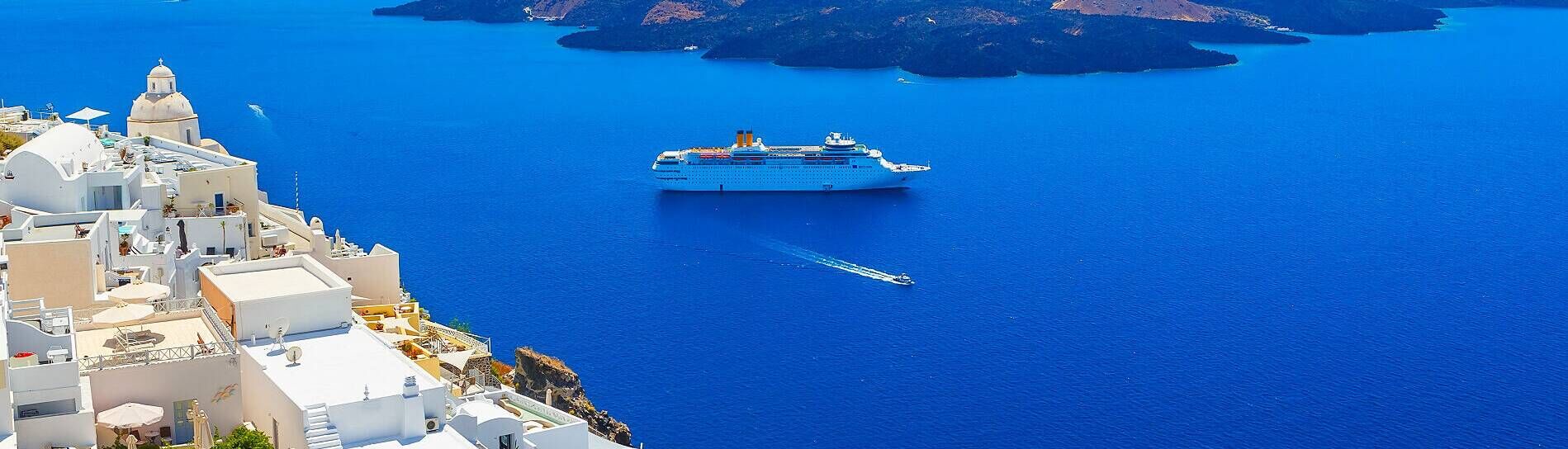 Kreuzfahrtschiff vor der Küste von Santorini mit weißen Häusern auf den Klippen und tiefblauem Meer in der Ägäis.