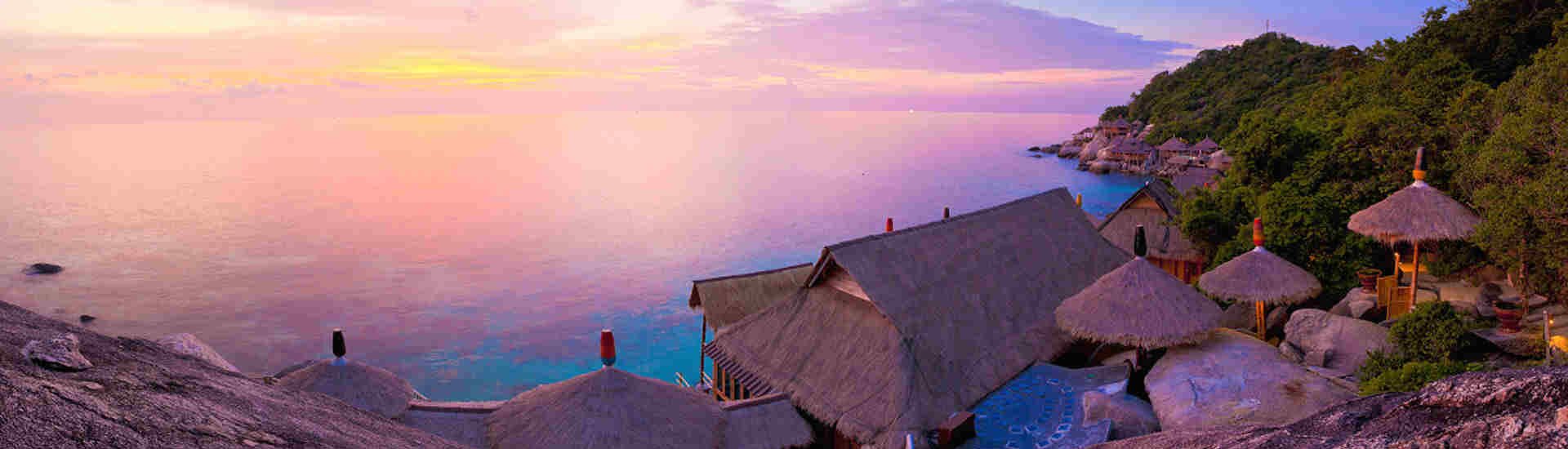 Sonnenuntergang über einer Bucht auf Koh Tao im Golf von Thailand mit traditionellen Bungalows am Hang