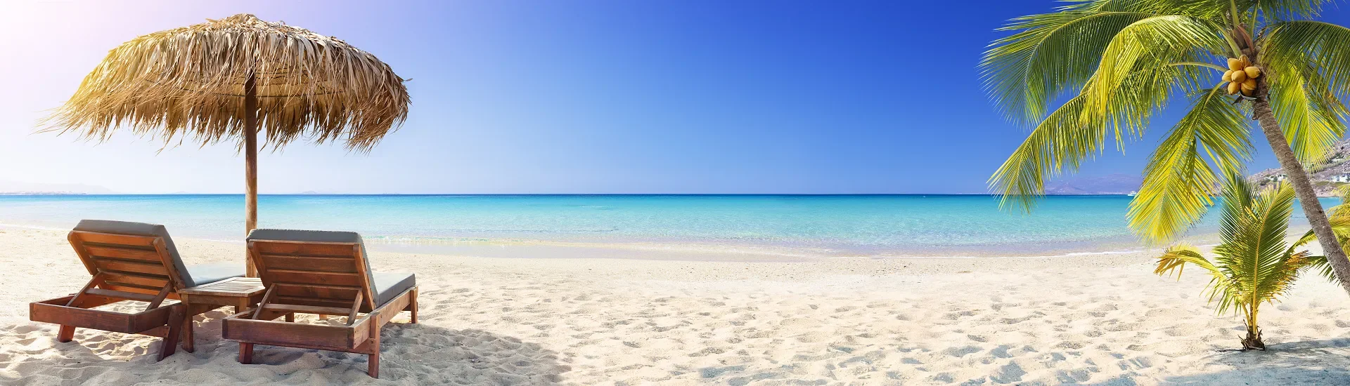 Zwei Liegen unter Sonnenschirm an tropischem Sandstrand mit Palmen und türkisfarbenem Meer in Asien