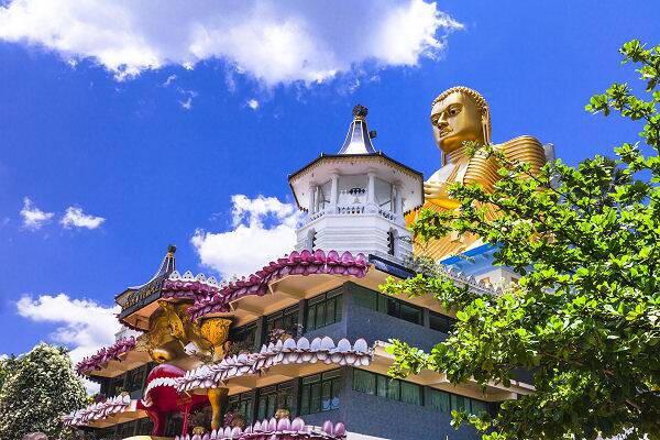 Buddhastatue und Tempelanlage in Sri Lanka vor blauem Himmel