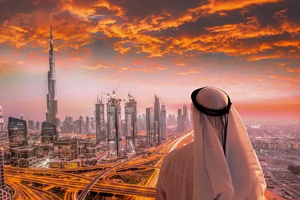 Skyline von Dubai mit Burj Khalifa bei Sonnenuntergang, Person vorn in traditioneller Kleidung