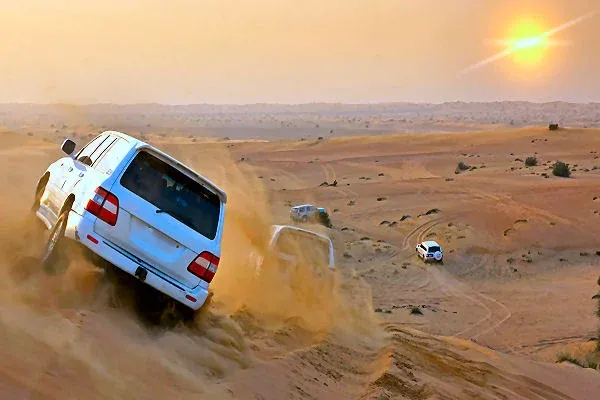 Geländewagen fahren durch die Wüste bei Sonnenuntergang in Dubai, Symbol für spannende Highlights