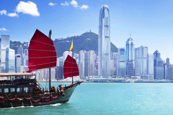 Traditionelle Dschunke mit roten Segeln im Victoria Harbour vor der Skyline von Hongkong