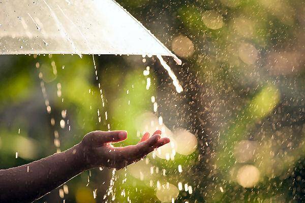 Regen fällt von einem Regenschirm auf eine ausgestreckte Hand – Symbol für Regenzeit in Thailand