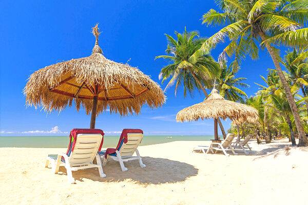 Sonnenliegen unter Strohdächern am Chaweng Beach auf Koh Samui mit Palmen und türkisfarbenem Meer