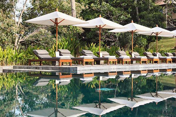 Sonnenliegen mit weißen Sonnenschirmen am Rand eines ruhigen Hotelpools in Asien