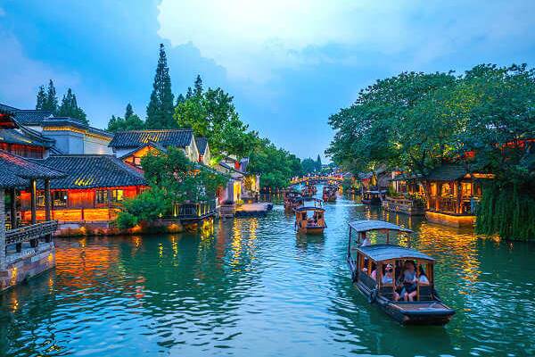 China Rundreisen – Wasserdorf Wuzhen bei Shanghai Traditionelles Wasserdorf Wuzhen bei Shanghai mit beleuchteten Häusern und Booten auf einem Kanal bei Abendlicht
