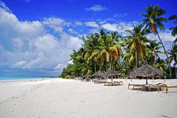 Weißer Sandstrand mit Palmen und Sonnenliegen auf Sansibar bei blauem Himmel