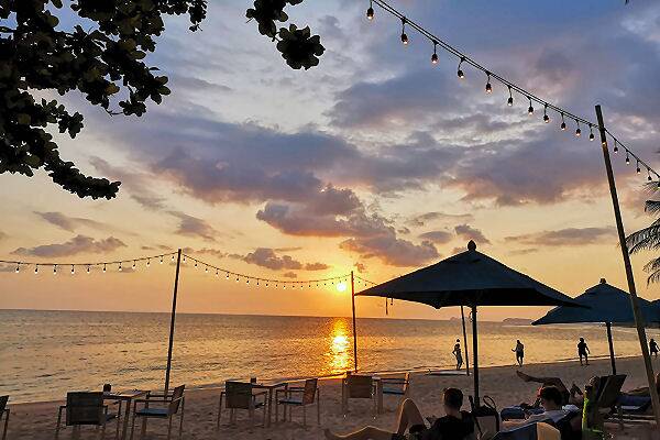 Strandbar auf Koh Phangan in Thailand bei Sonnenuntergang mit Blick auf das Meer, beleuchteten Lichterketten und entspannter Atmosphäre am Sandstrand.