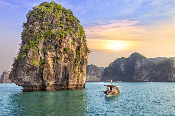 Kalksteinfelsen und Boot in einer Bucht in Thailand bei Sonnenuntergang