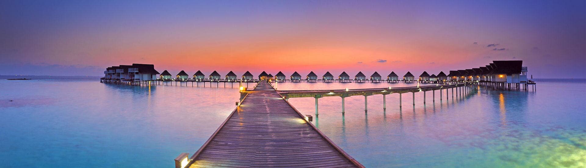 Resortsteg mit Wasserbungalows auf den Malediven bei Sonnenuntergang über türkisfarbener Lagune
