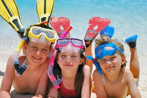 Drei Kinder mit Taucherbrillen und Flossen liegen lachend am Strand und genießen den Urlaub in Dubai