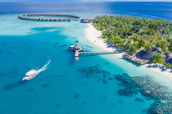 Blick auf Wasserbungalows und Boot im türkisfarbenen Meer, Symbol für Malediven Urlaub