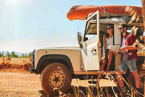 Ein Paar steht mit Karte neben einem Geländewagen auf staubiger Straße und plant eine Rundreise mit AsiaGo