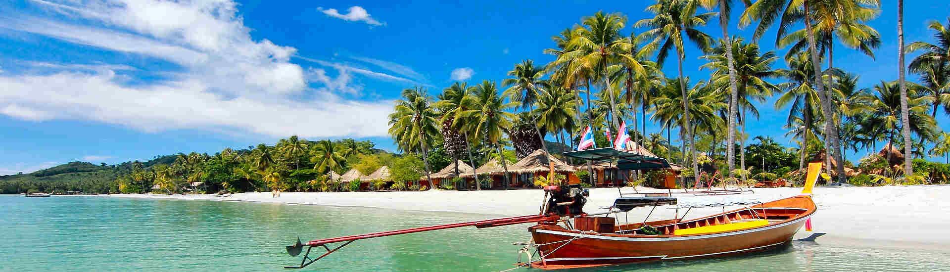 Weißer Sandstrand auf Koh Chang mit Palmen, traditionellen Bungalows und Longtailboot im türkisfarbenen Wasser