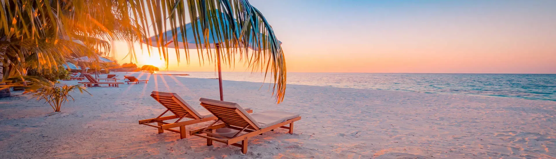 Zwei Sonnenliegen unter Palmen am Strand bei Sonnenuntergang