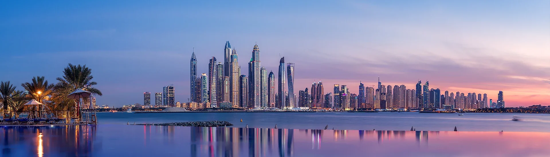 Skyline einer modernen Metropole in den Vereinigten Arabischen Emiraten am Wasser bei Sonnenuntergang