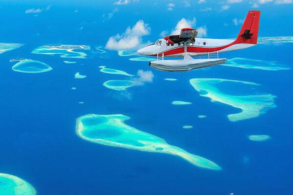 Wasserflugzeug fliegt über Inseln und Lagunen im Indischen Ozean