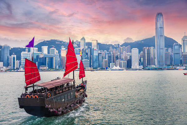 Segelschiff im Hafen von Hongkong vor der Skyline bei Sonnenuntergang