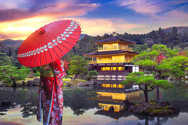Traditionell gekleidete Frau mit rotem Schirm vor dem Goldenen Pavillon Kinkaku-ji in Kyoto, Japan.