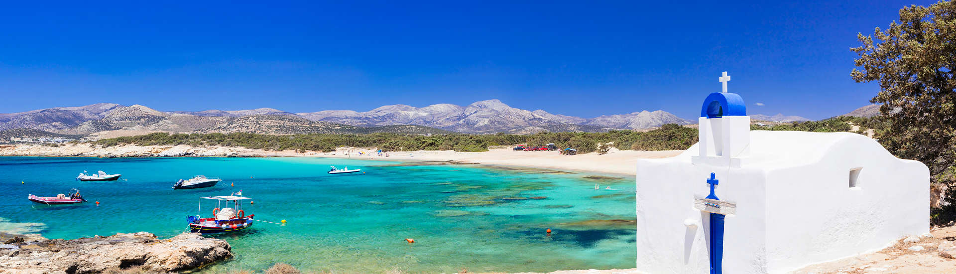 Griechenland Urlaub – Entspanne an den traumhaften Stränden von Naxos Malerische Bucht auf Naxos mit klarem Wasser und einer traditionellen weißen Kapelle am Strand